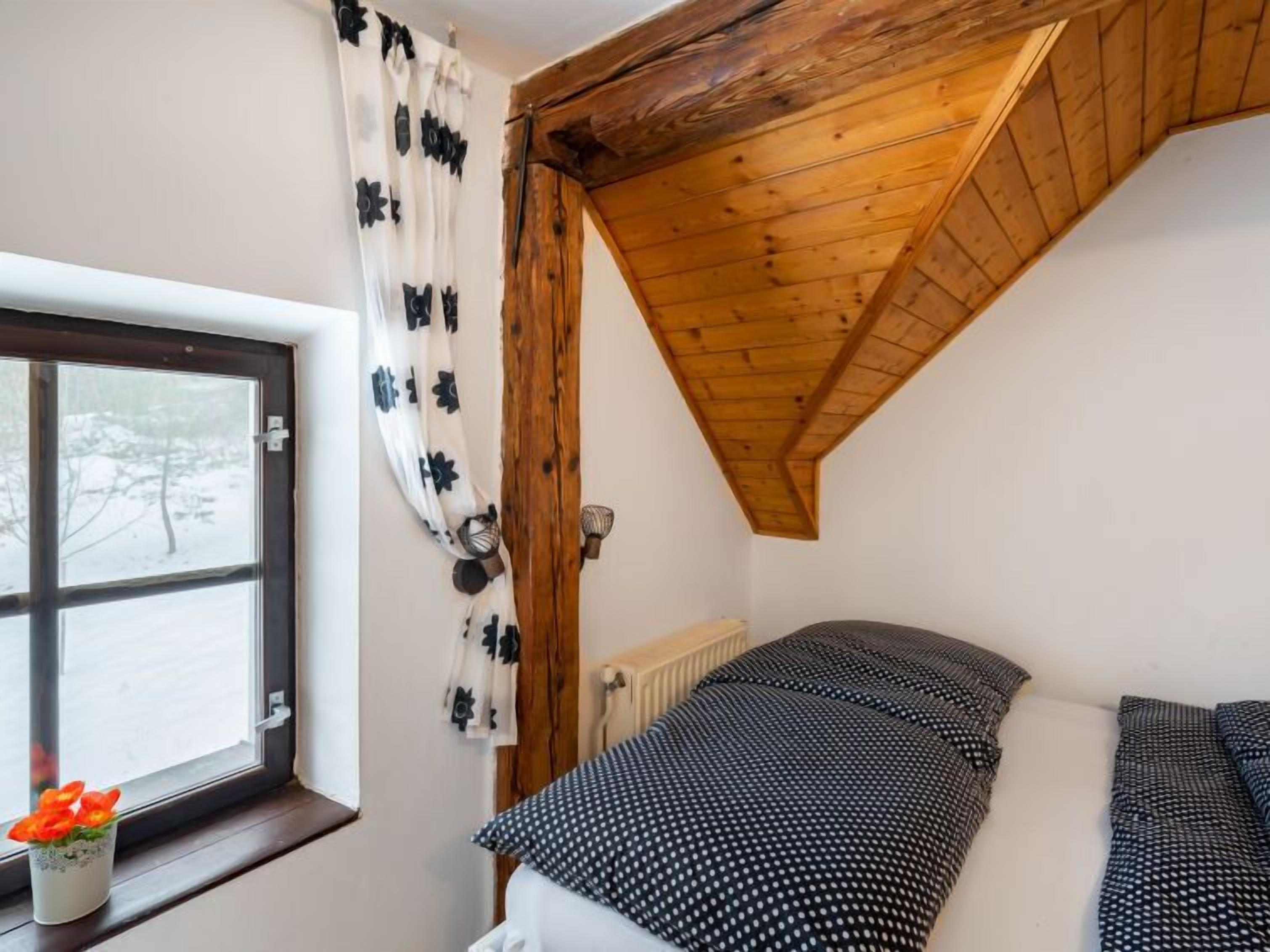 Ein Schlafzimmer mit Holzbalkendecke, einem Fenster mit Blick auf schneebedeckte Bäume und einem Bett mit einem Punkte-Bettbezug.