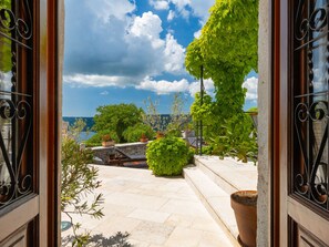 Un umbral abierto que da a una terraza con suelo de piedra, plantas en macetas y vistas al mar.