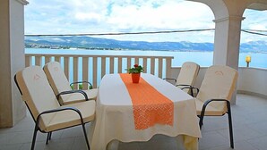 A terrace with a table and chairs, a potted plant, and a view of a lake and mountains. - Apartment Mornar by Interhome (Trogir/Arbanija)