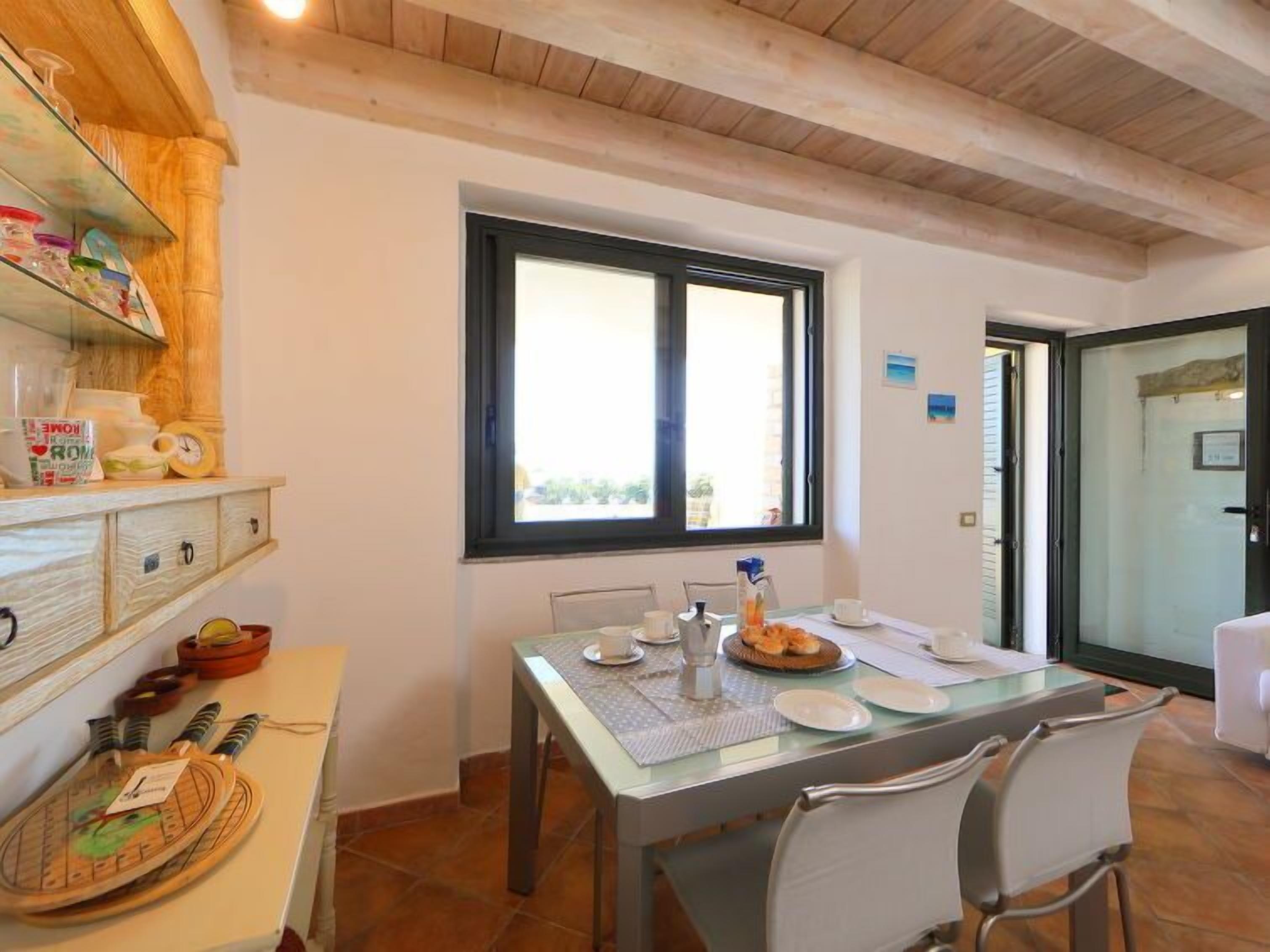 Un comedor con una mesa dispuesta para dos, una ventana con vistas y una zona de cocina con armarios y utensilios.