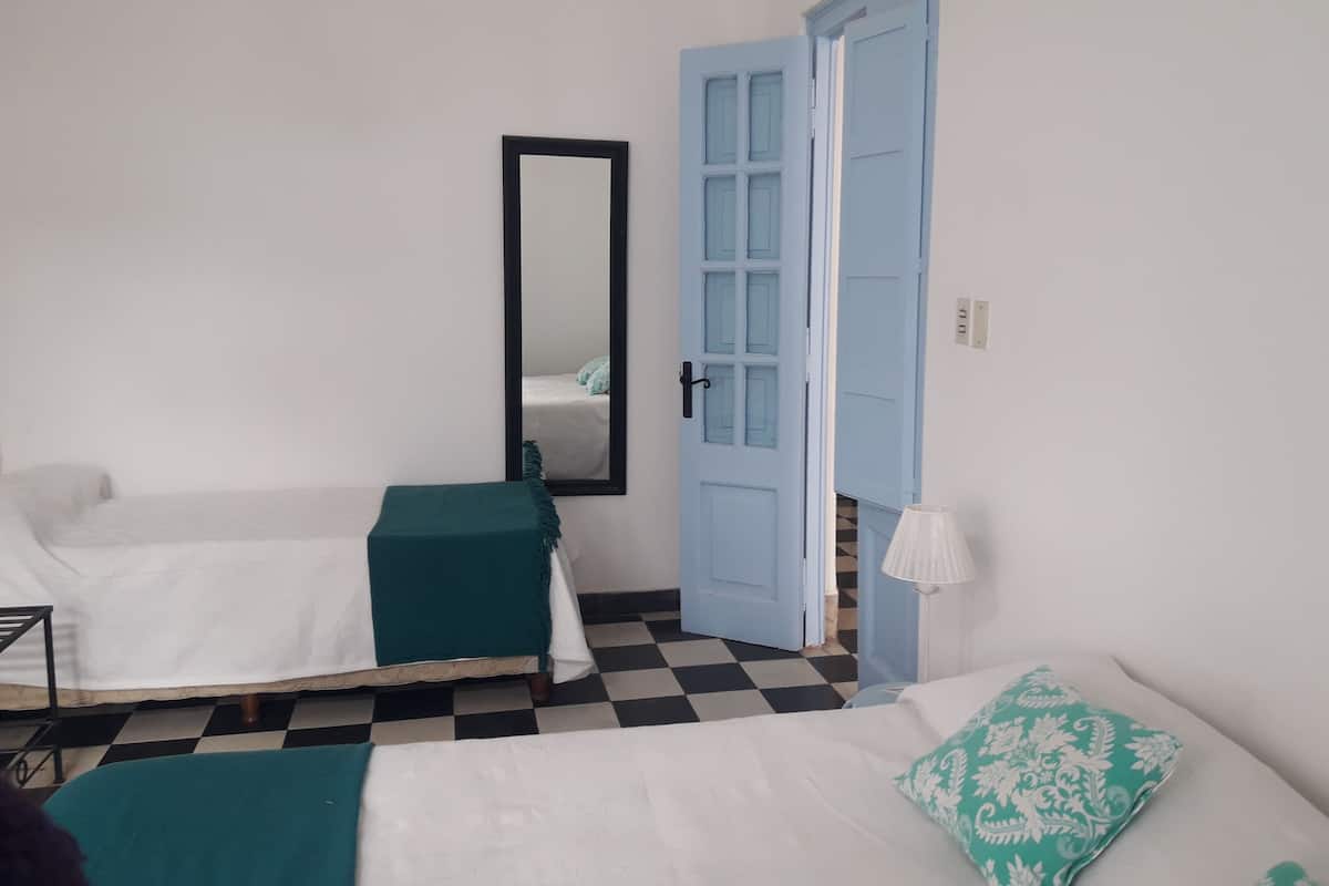A room with two beds, a mirror, a blue door, and a checkered floor.