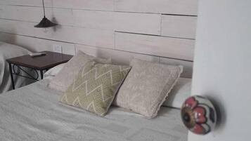 Quarto com cabeceira de madeira, cama com roupa de cama estampada, mesa de cabeceira e abajur.