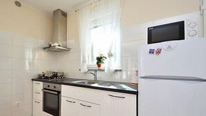 Et moderne køkken med hvide skabe, en sort bordplade, en komfur, en vask og et hvidt køleskab.