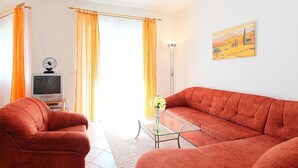 A living room with two red sofas, a glass coffee table, a television, and a painting on the wall.