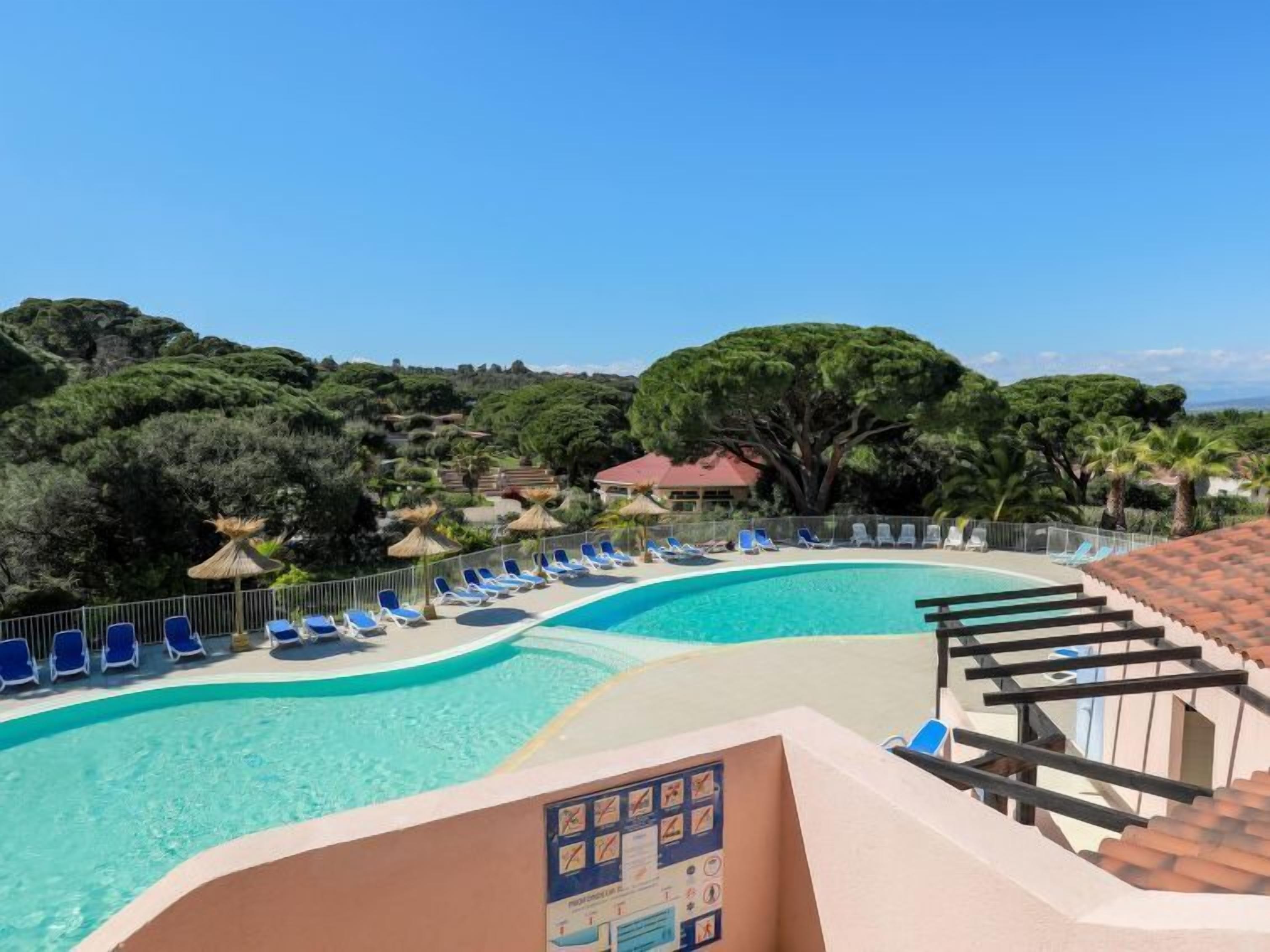 Une piscine avec des chaises longues bleues et un panneau indicateur.