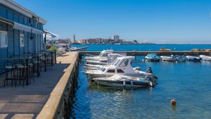 Un port de plaisance où sont amarrés plusieurs bateaux, un bâtiment doté d’une terrasse, et un ciel d’un bleu limpide.