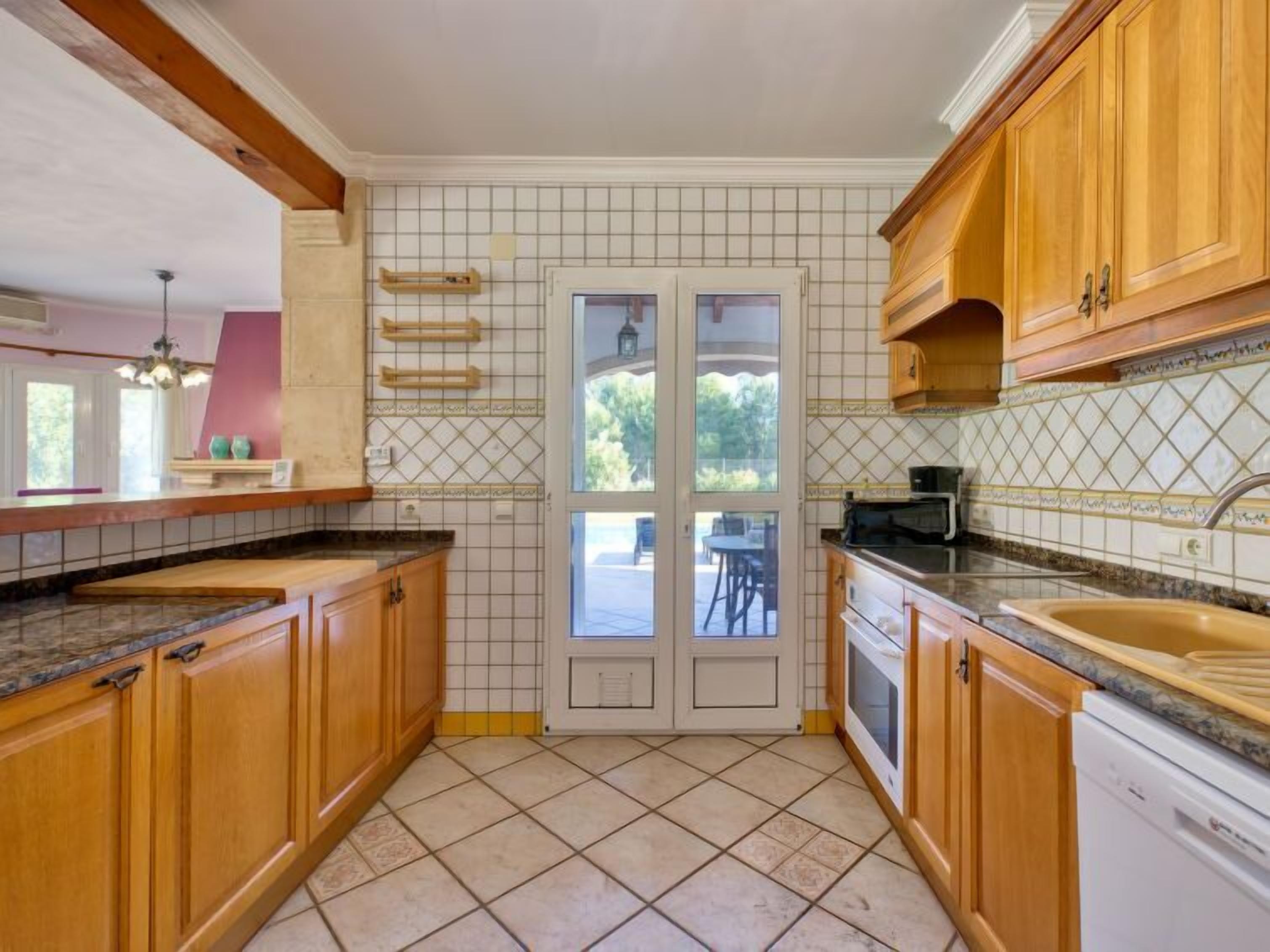 Una cocina con armarios de madera, salpicadero de azulejos y un ventanal grande.