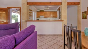 Een keuken met houten kastjes, een betegelde spatwand en een eethoek met een tafel en stoelen.