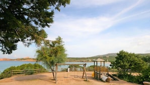 A sandy outdoor area with a swing set, a gazebo, and a view of a lake and hills.