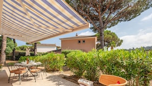 Une terrasse extérieure dotée d’un auvent à rayures, d’une table dressée pour le repas, de chaises en osier et d’une petite table avec un plateau.