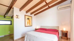 Un dormitorio con cama, mesitas de noche, un cuadro y una ventana.