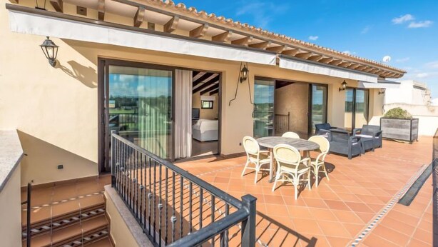 Una terraza en la azotea con zona de comedor, un ventanal corredero que da a un dormitorio y suelo de baldosas.
