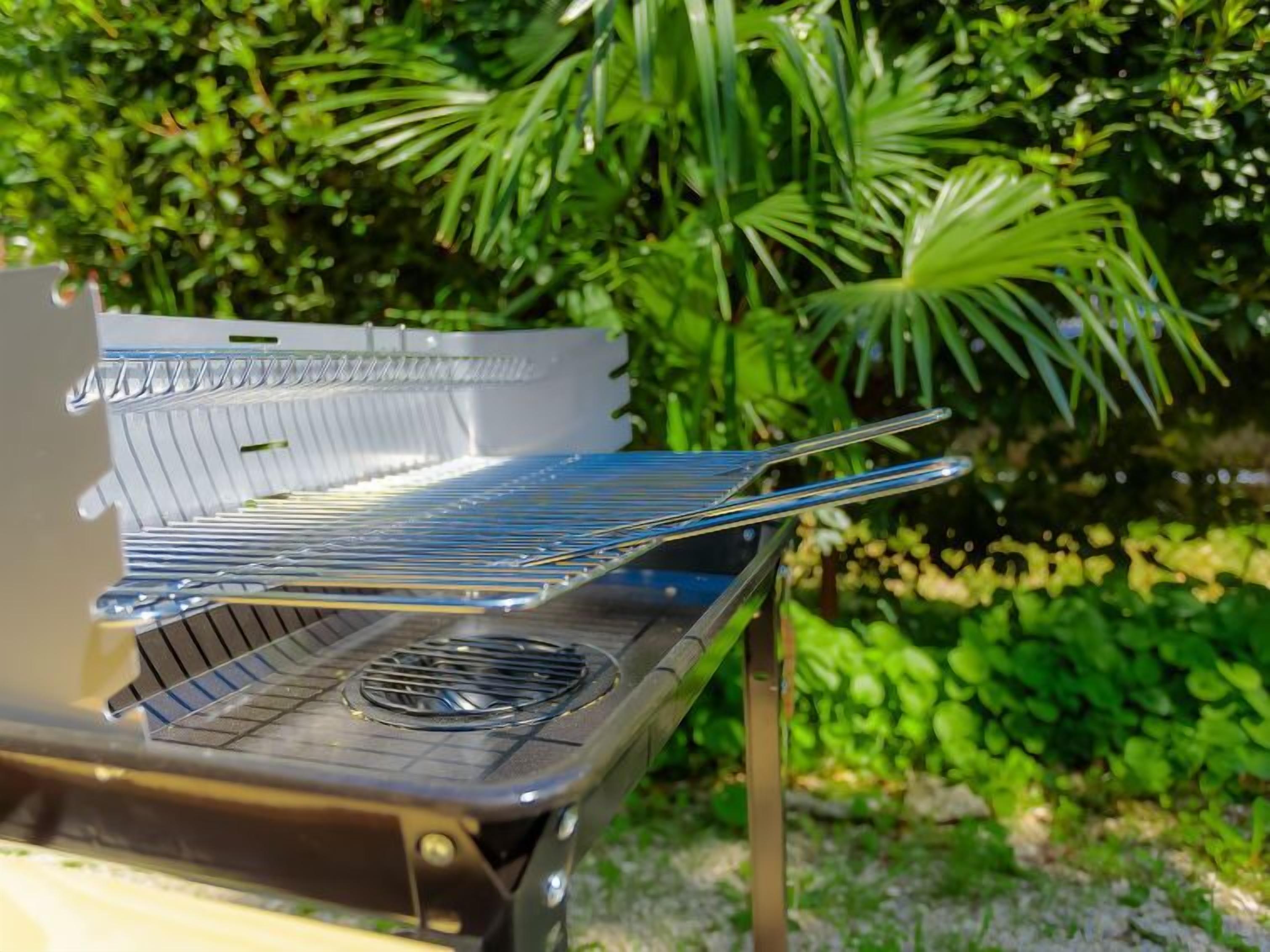 A portable grill with a metal rack and a vent, set outdoors with greenery in the background.