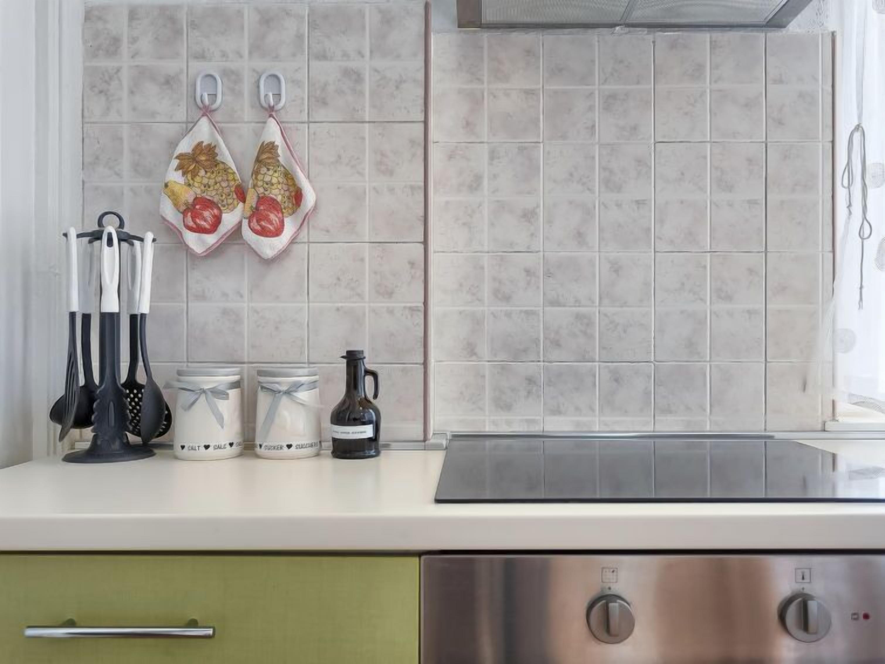 A kitchen with a stainless steel stove, a green cabinet, and a tiled backsplash.