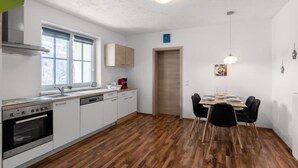 Une cuisine moderne avec des meubles blancs, un four encastré et un coin repas comprenant une table et des chaises.