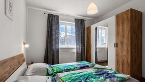 Une chambre avec une tête de lit en bois, un lit avec une literie verte et blanche, un luminaire suspendu et un grand miroir.