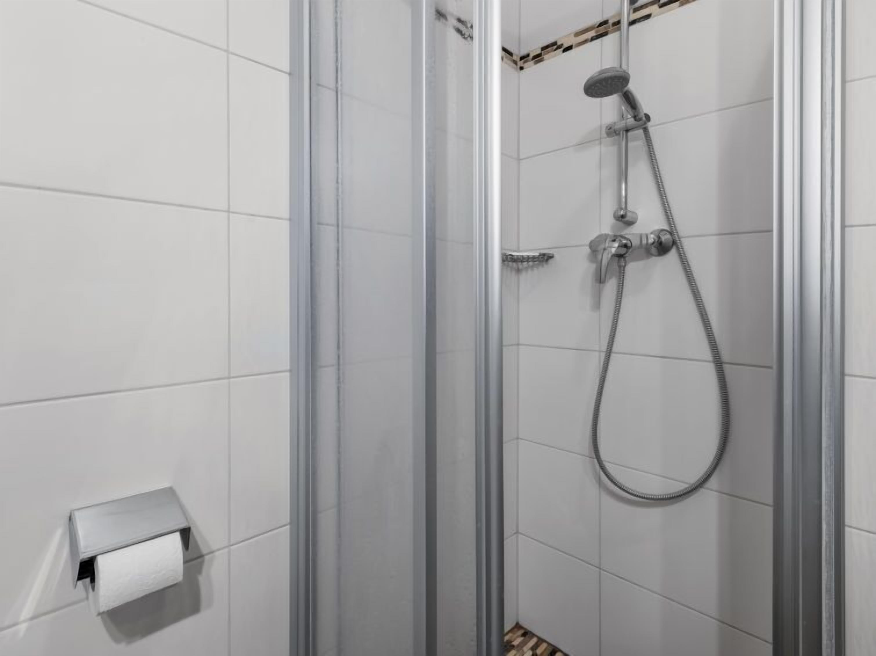 A modern shower with a glass door, a handheld showerhead, and a wall-mounted faucet.