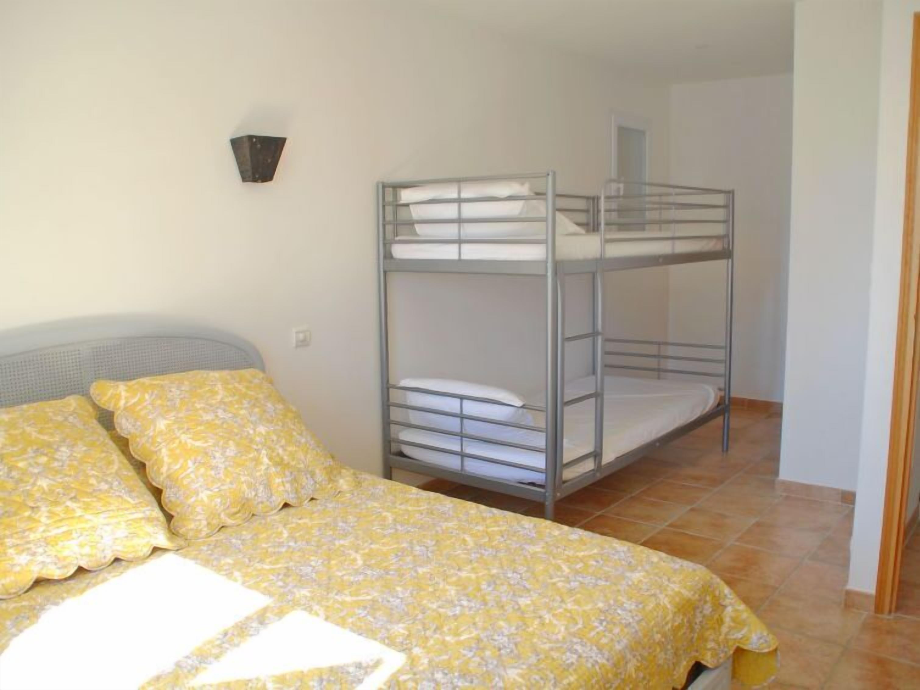 A bunk bed room with a single bed and two pillows, a wall-mounted light, and a tiled floor.