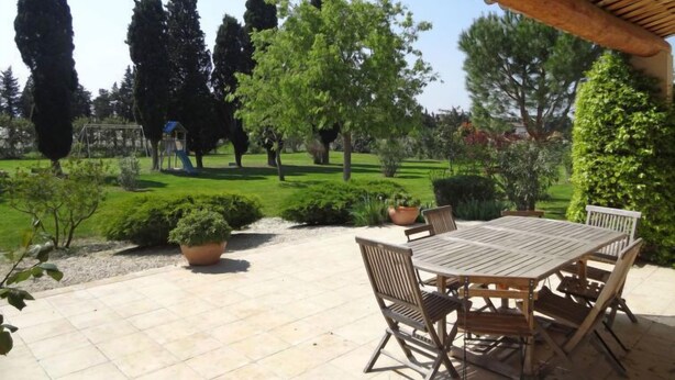 An outdoor patio with a wooden table and chairs, surrounded by potted plants and a well-maintained lawn. - Siflora by Interhome (Saint-Rémy-de-Provence)
