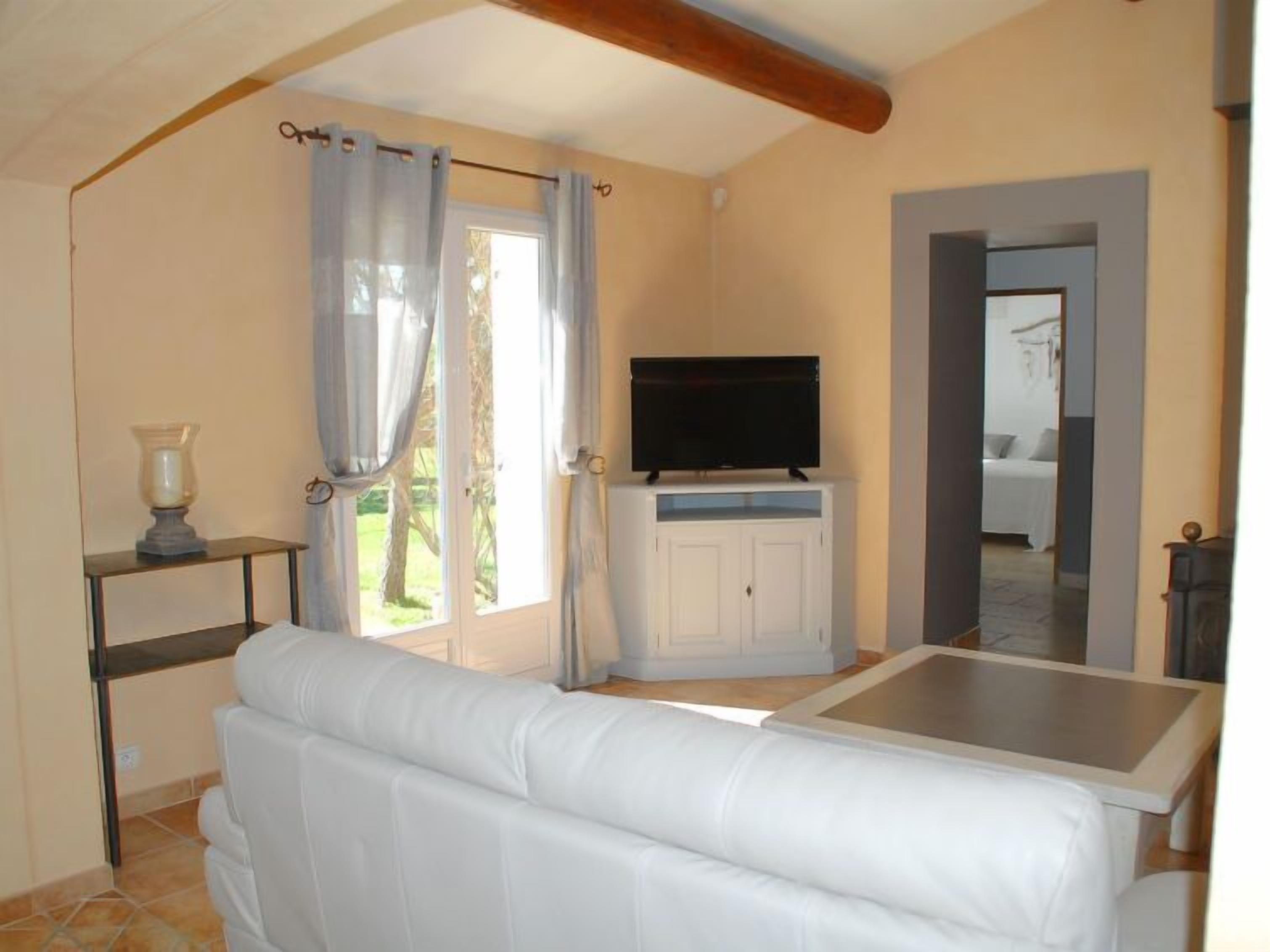 A room with a white sofa, a television on a cabinet, and a door leading to another room.