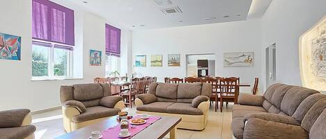 A spacious living room with multiple sofas, a dining area, and artwork on the walls.