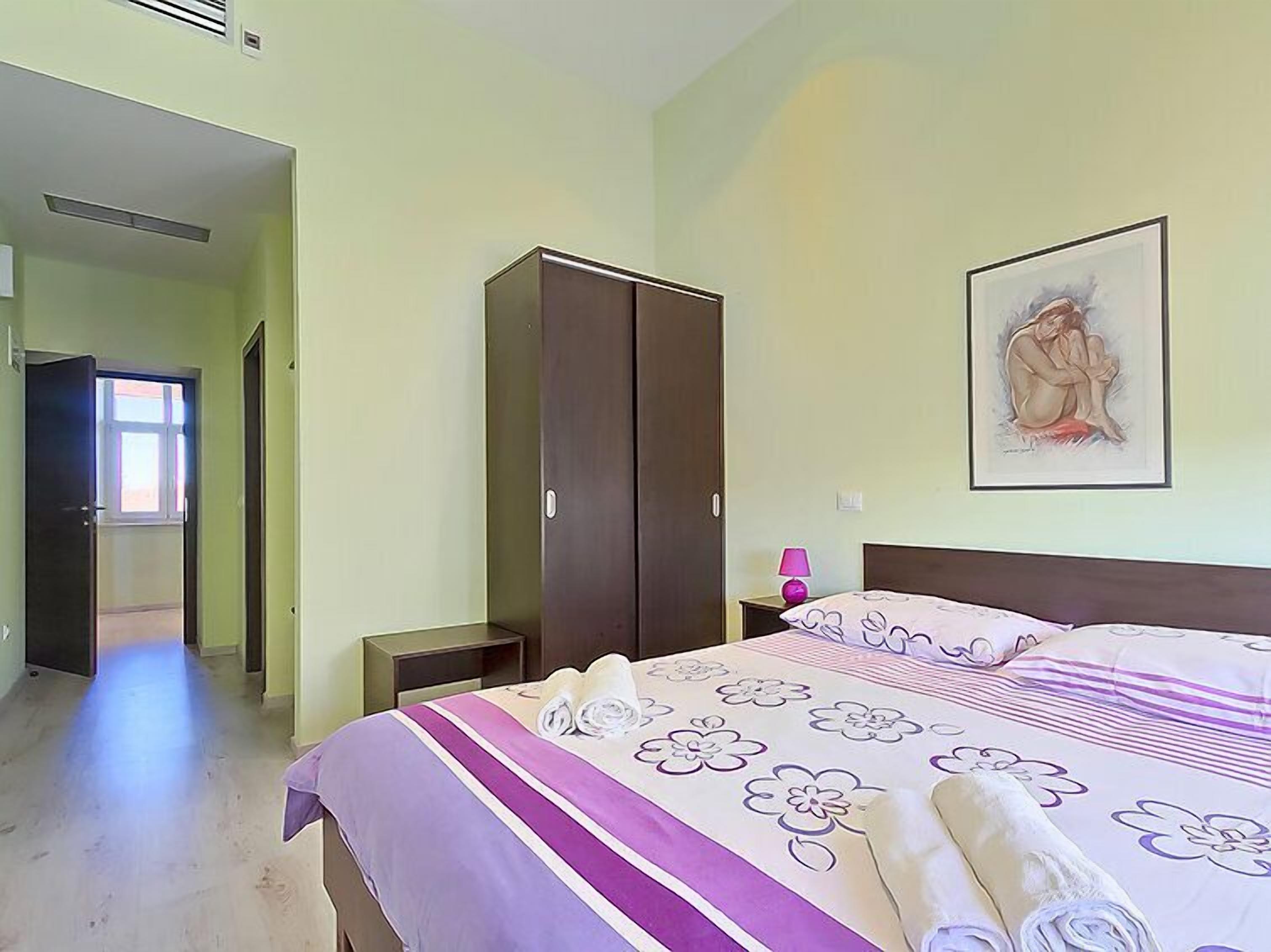 A bedroom with a bed, a wardrobe, a nightstand, and a painting on the wall.