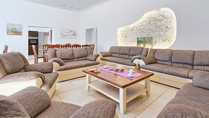 A spacious living room with a large stone wall, a dining area with wooden furniture, and a kitchen in the background.