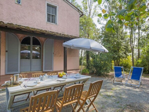 Un área de comedor al aire libre con una mesa preparada para cuatro personas, rodeada de sillas de madera.
