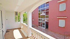 A covered outdoor area with a tiled floor, white railings, and a red building with multiple windows and shutters. - Apartment Tino by Interhome (Pag/Pag)