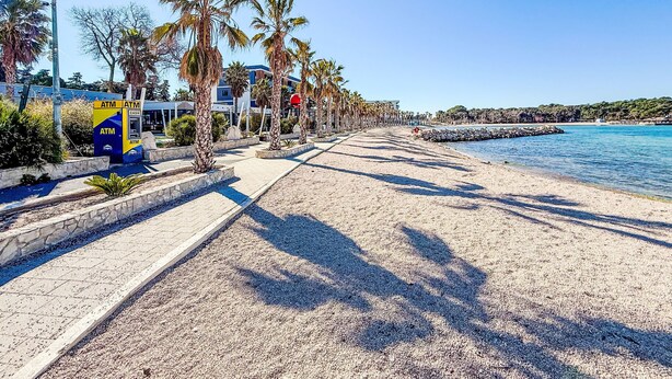 A beachside promenade with palm trees, a sandy path, and a calm sea. - Apartment Tino by Interhome (Pag/Pag)