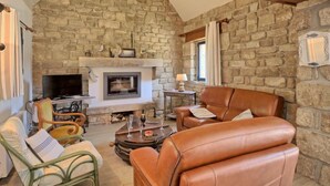 A cozy living room with a stone fireplace, leather sofa, and a television. - St Adrien by Interhome (Ploemeur)