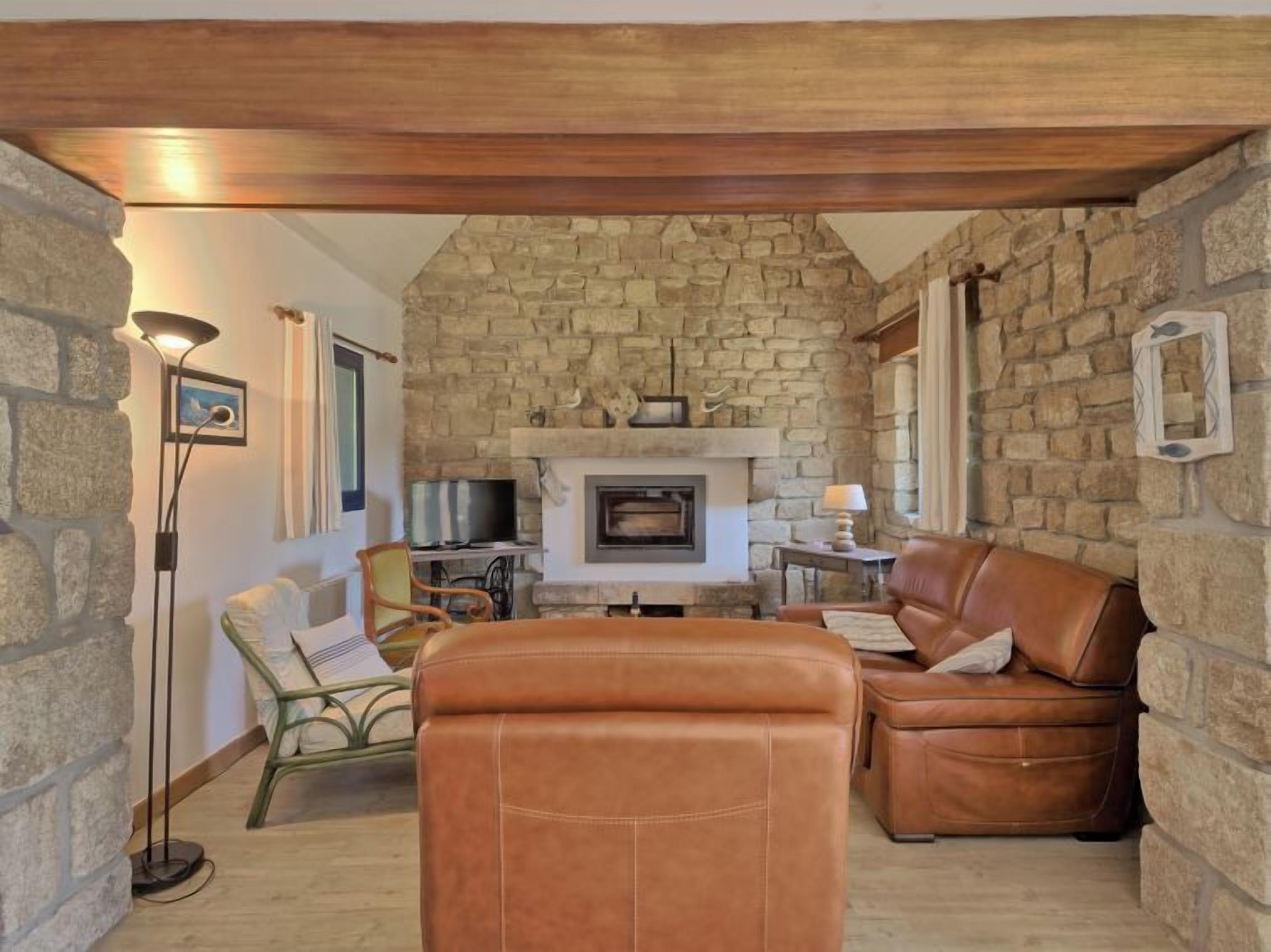 A cozy living room with stone walls, a fireplace, leather sofas, and a television.