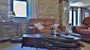 A stone-walled room with a brown leather sofa, a wooden coffee table with a bottle and glass, and a lamp on a side table. - St Adrien by Interhome (Ploemeur)