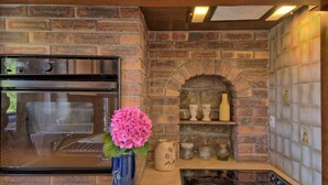 A kitchen with a brick wall, a built-in oven, a stove, and a shelf with decorative items. - St Adrien by Interhome (Ploemeur)