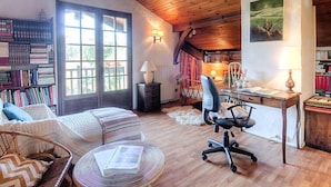 Una habitación acogedora con techo de madera, un ventanal grande, una estantería, un escritorio con una silla y un cuadro en la pared.