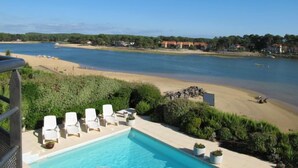 A pool area with lounge chairs and a view of a beach and water body. - Les Pinasses by Interhome (Mimizan)