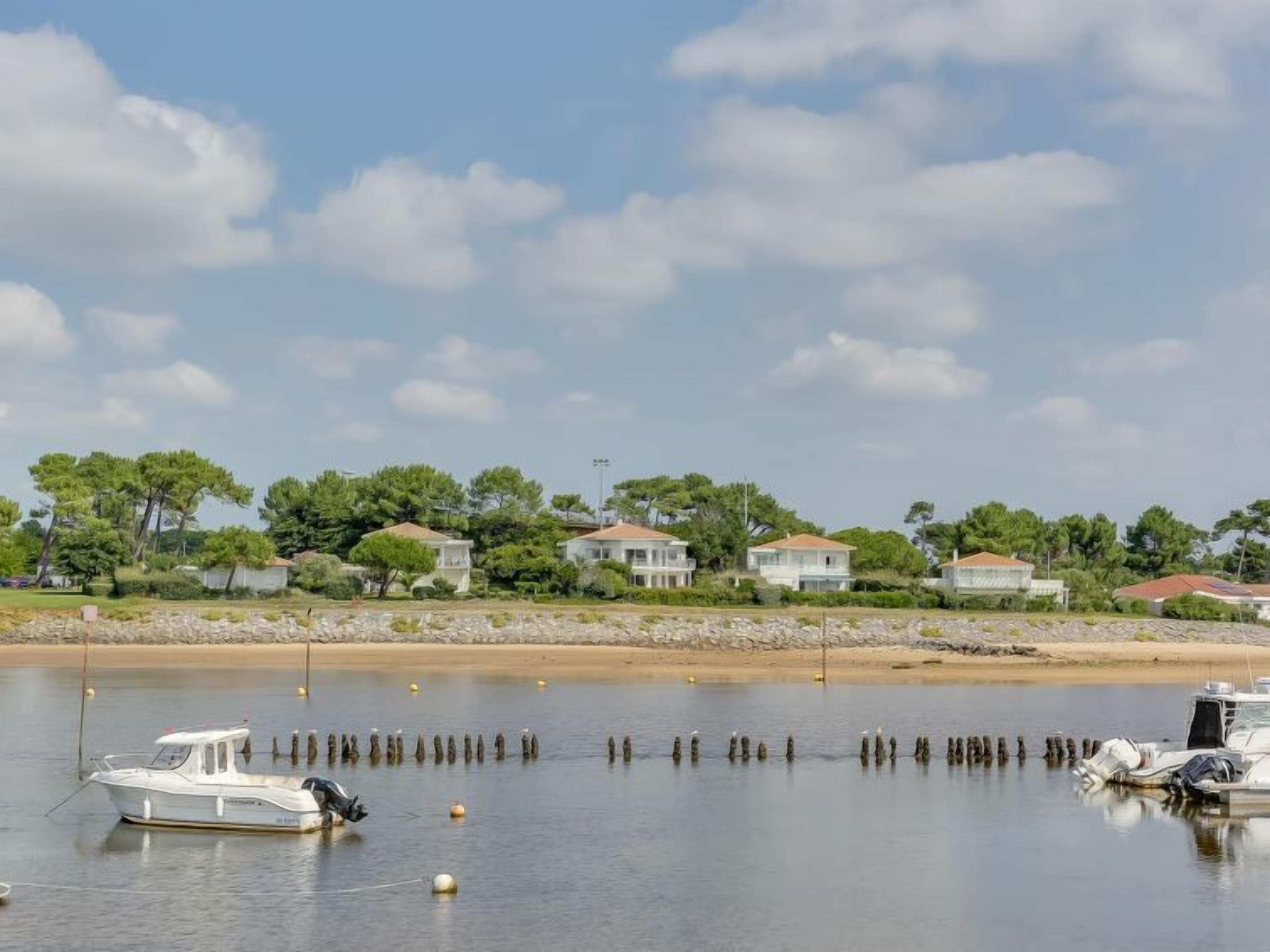 A calm waterfront with a row of houses, a boat docked near the shore, and a clear sky.