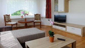 Uma sala de estar com sofá, duas poltronas, uma mesa de centro, televisão e um pequeno armário.