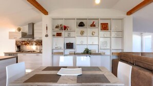 A modern kitchen with white cabinetry, a built-in island, and a dining area with a wooden table and white chairs. - Vacation home Finida by Interhome (Umag)