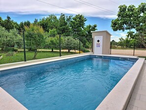 A rectangular swimming pool with a tiled edge, surrounded by a fence and trees.