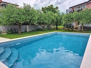 A rectangular swimming pool with clear blue water, surrounded by a well-maintained lawn and trees.