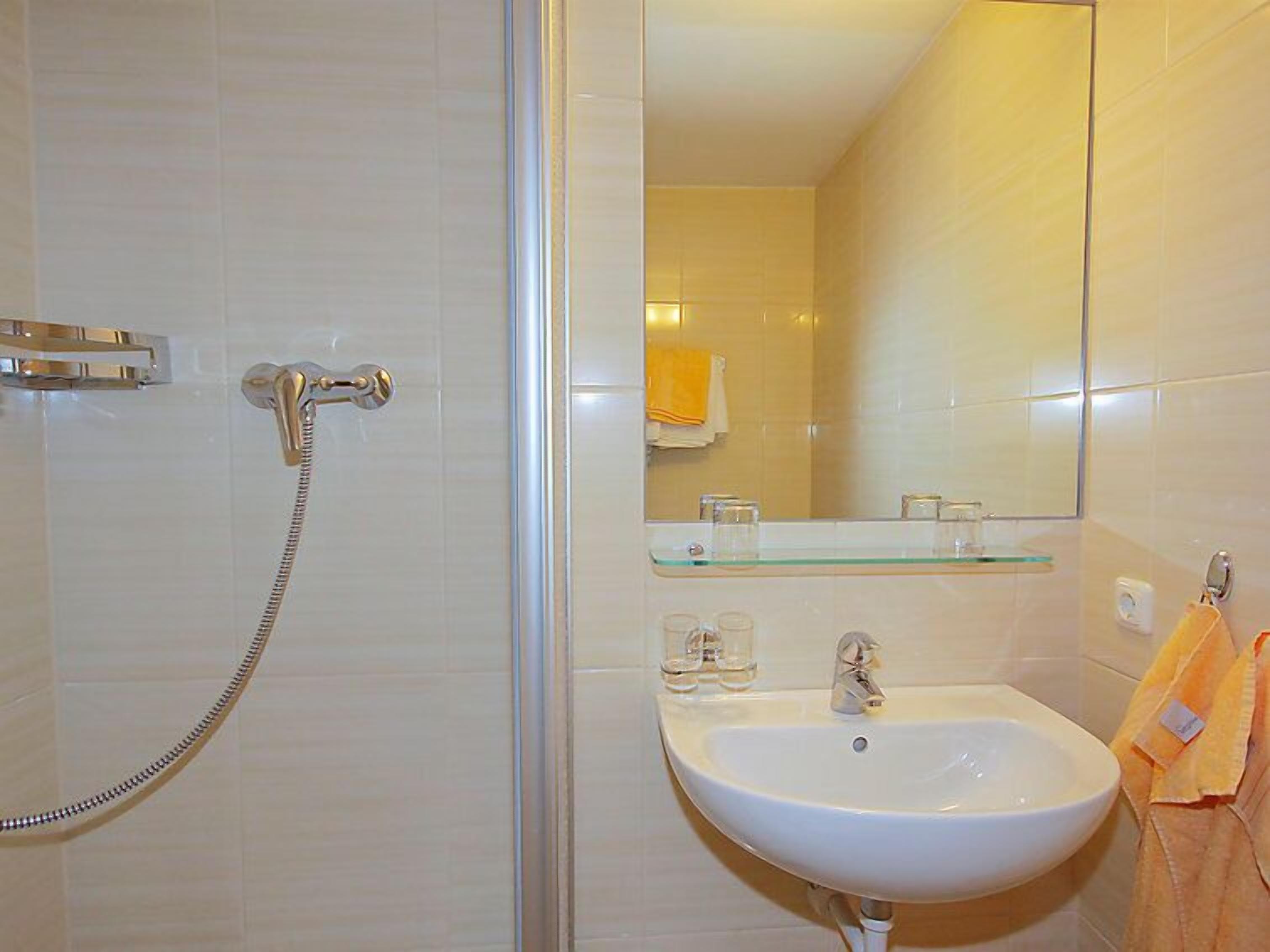 Un bany amb plat de dutxa de vidre, un lavabo blanc i un mirall.