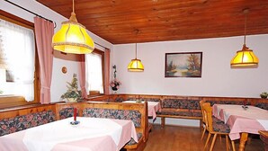 Un comedor con bancos y mesas de madera, lámparas colgantes amarillas y un cuadro en la pared.