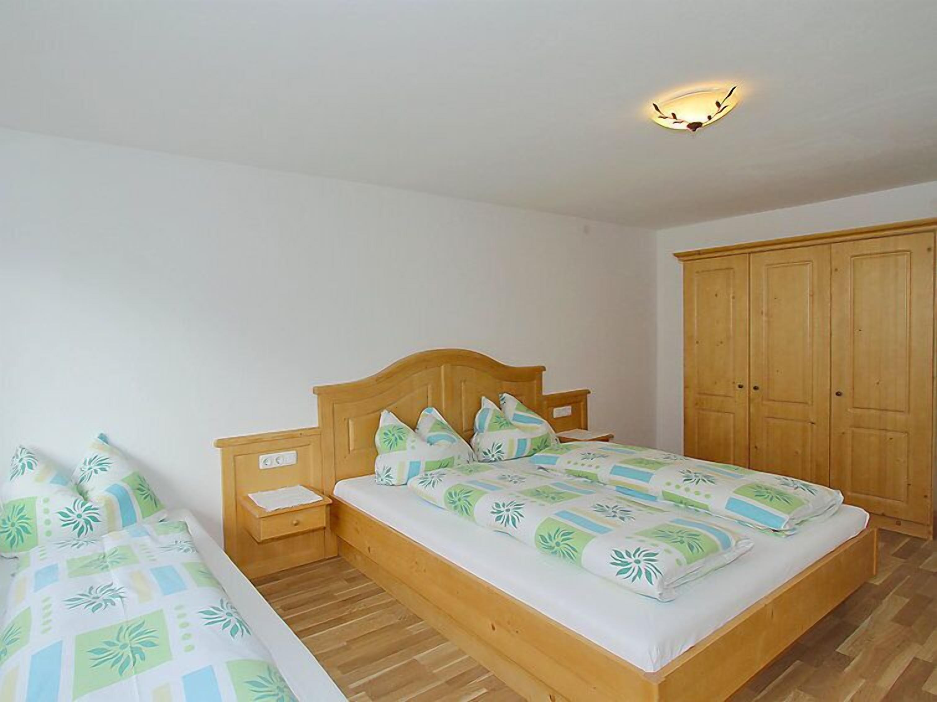 Une chambre à coucher avec un lit en bois, une table de chevet, une armoire et un luminaire au plafond.