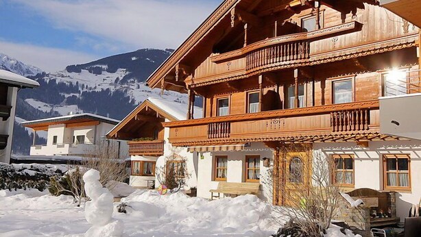 Una cabaña de madera con balcones, con una imponente montaña nevada al fondo.