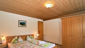 Un dormitorio con una cama de madera, dos mesitas de noche con lámparas, un armario de madera y una lámpara en el techo.