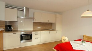 Una cocina compacta con horno integrado, cafetera y comedor con mantel rojo.
