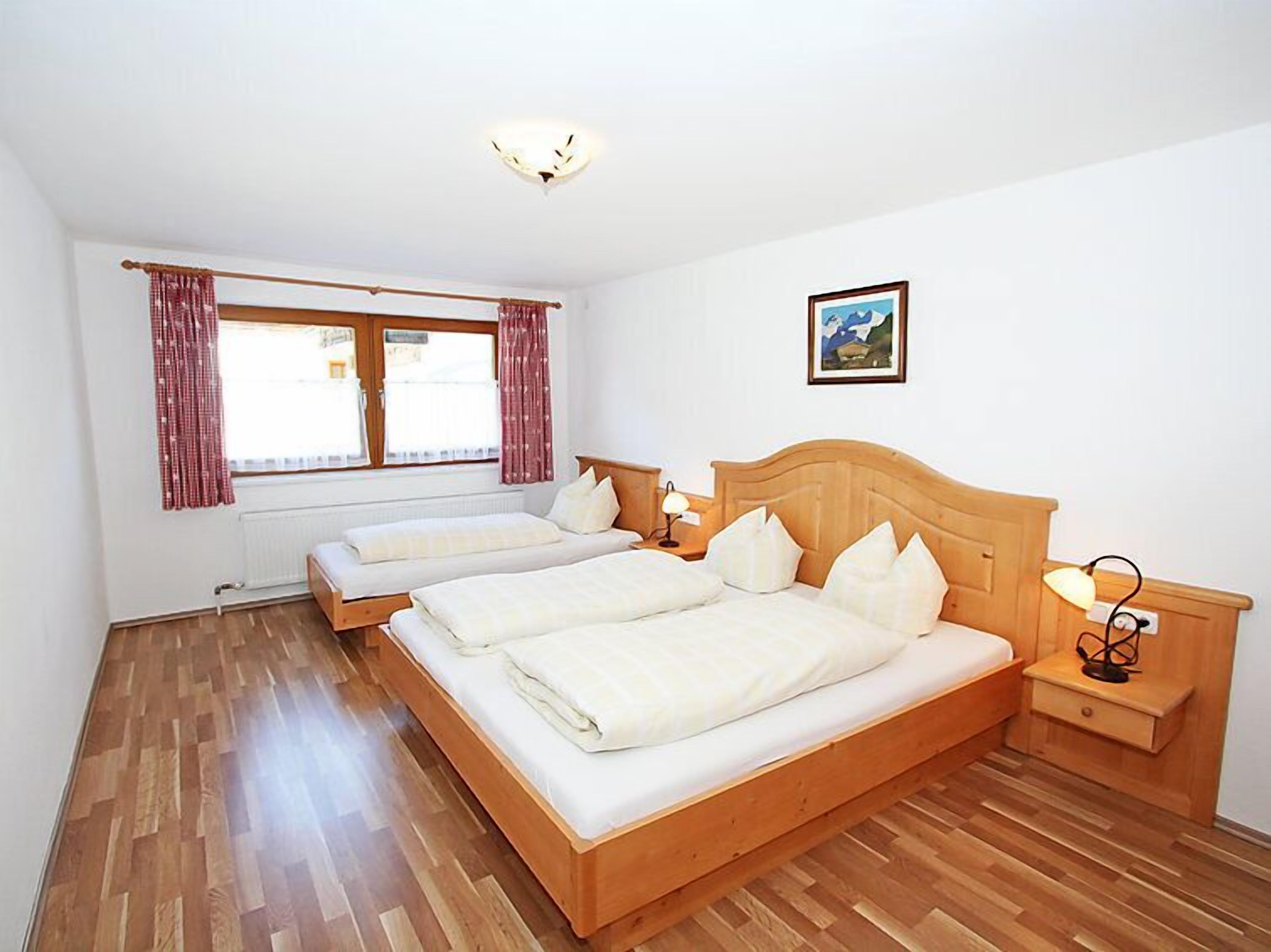 Een tweepersoonskamer met twee bedden, een raam met gordijnen, een nachtkastje met een lamp en een lijst met een afbeelding aan de muur.