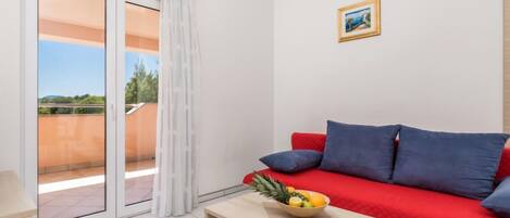 A modern living room with a red sofa, a wooden coffee table with a fruit bowl, and a sliding glass door leading to a balcony.