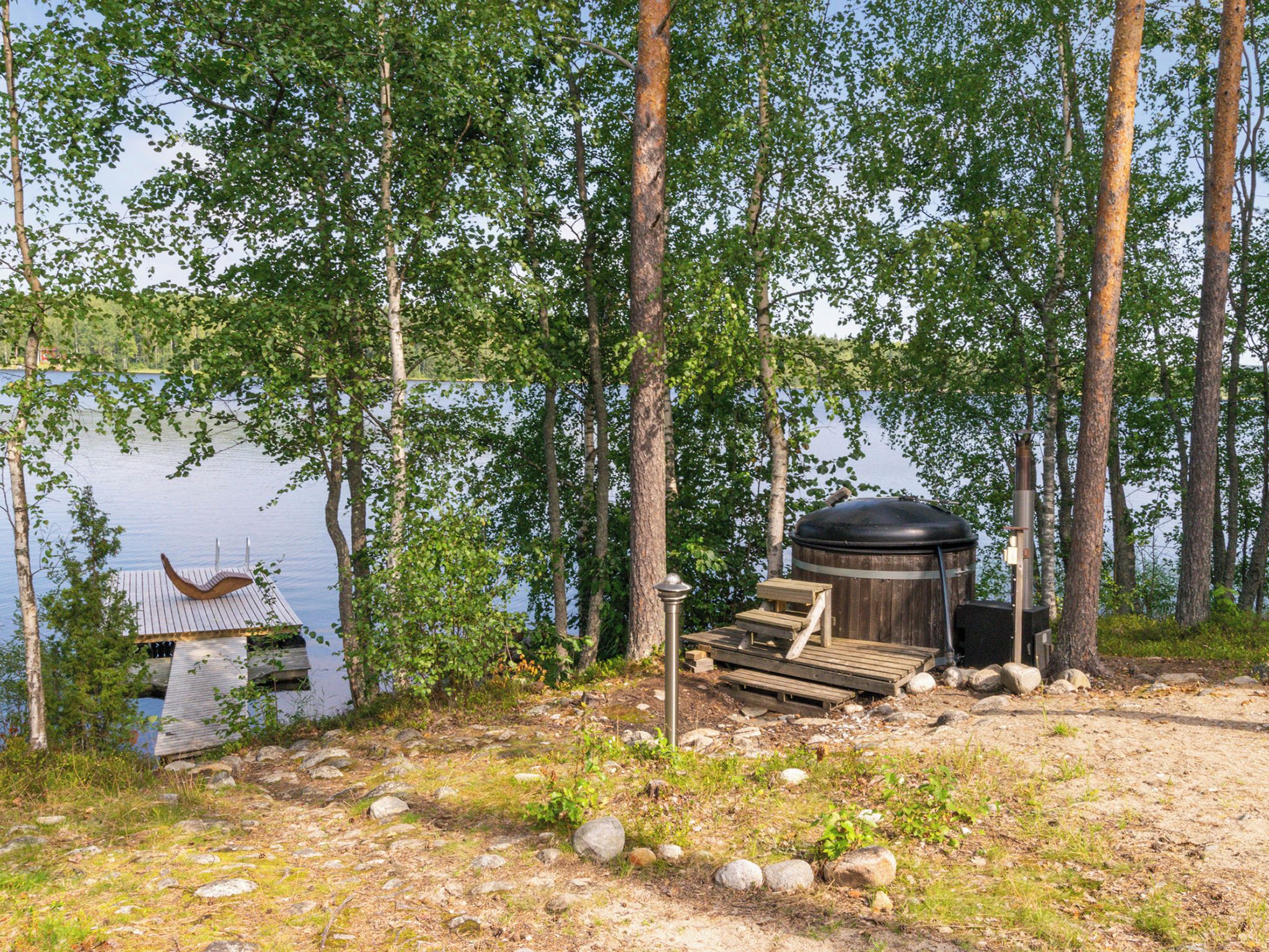 A lakeside cabin with a dock, a sauna, and a wooden deck.